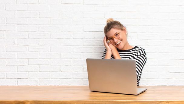 young pretty latin woman feeling in love and looking cute, adorable and happy, smiling romantically with hands next to face sitting with her laptop - Фото, изображение