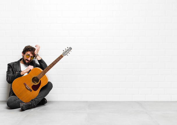 young musician man feeling stressed and anxious, depressed and frustrated with a headache, raising both hands to head with a guitar, rock and roll concept - Foto, Bild
