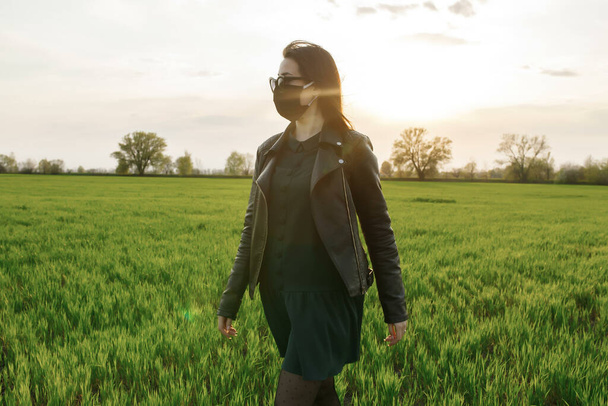 Una chica con una máscara médica corre o camina en un campo verde. Cuarentena primavera verano. coronavirus. COVID 19. Virus de la gripe, resfriados - Foto, imagen
