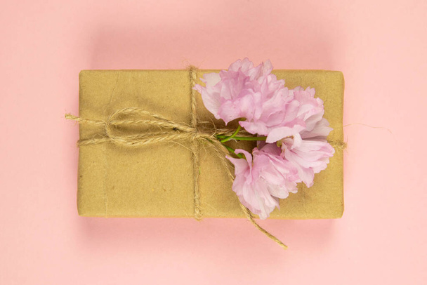 Gift boxes wrapped of craft paper and burlap ribbon with pink flowers on the pink background, top view, close-up. - Φωτογραφία, εικόνα
