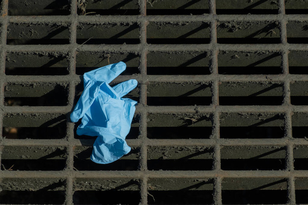 Ένα προστατευτικό γάντι εγκαταλελειμμένο σε μια σχάρα στο δρόμο. Απορρίφθηκε μετά τη χρήση. - Φωτογραφία, εικόνα