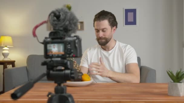 Nuori mies, vlogger tekee videon, hän istuu pöydässä kameran edessä ja puhuu hedelmistä ja niiden eduista.
 - Materiaali, video