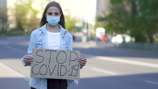 Giovane donna in maschera medica protesta con poster Stop covid 19 sulla strada della città. Squadra pandemica, rallentatore
. - Filmati, video