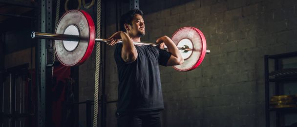 ázsiai erős sportos férfi miután edzés és testépítés súlyzós súlyzós elülső guggolás beállítás stílus tornaterem és fitness klub sötét tónusú - Fotó, kép