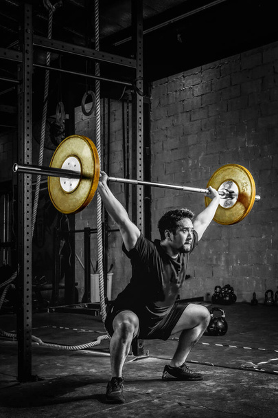 asian strong athletic man having workout and bodybuilding with barbells weight lift over head squat style in gym and fitness club in dark two tone - Fotoğraf, Görsel