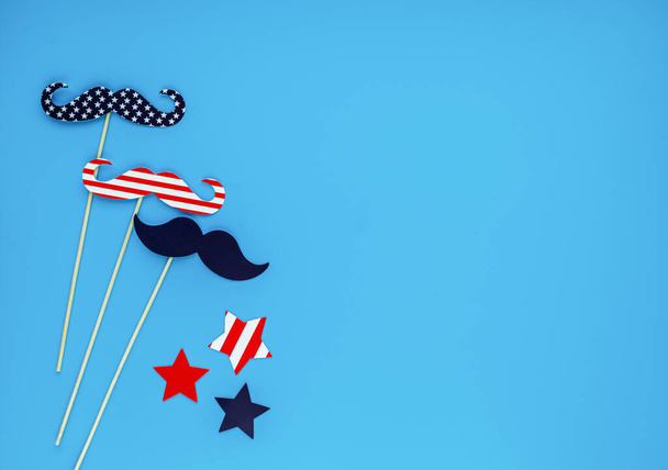 Fotohokje voor 4 juli. Snor, lippen, bril, hoed op stokken op blauwe achtergrond. Amerikaanse vlag kleuren. Onafhankelijkheidsdag, patriottische vakantie achtergrond. - Foto, afbeelding