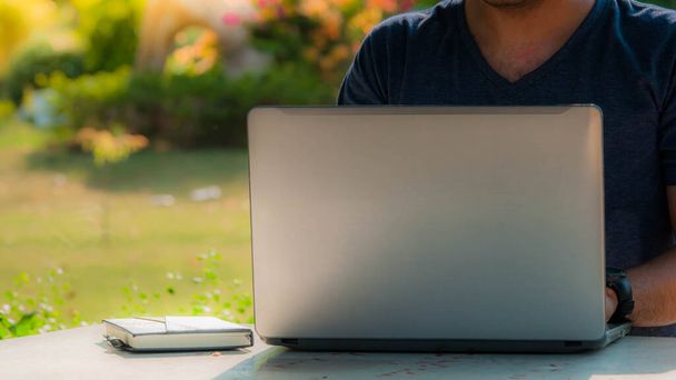 Una persona que trabaja o aprende en línea por computadora portátil en el escritorio en el jardín de la casa
. - Foto, Imagen
