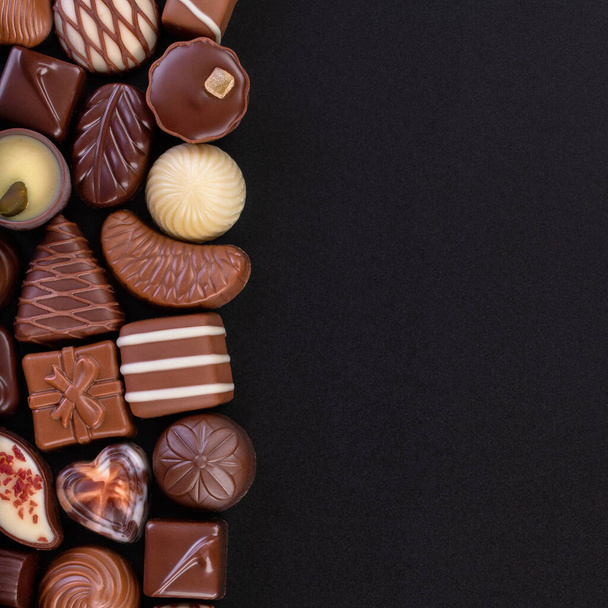 Siyah masa zemininde beyaz ve siyah çikolatalardan oluşan çeşitli şekerler. - Fotoğraf, Görsel
