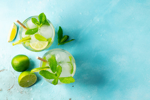 Zwei hausgemachte Limonaden oder Mojito-Cocktails mit Limetten, Minze und Eiswürfeln im Glas auf einem hellen Steintisch. Frisches Sommergetränk. Draufsicht mit Kopierraum. - Foto, Bild