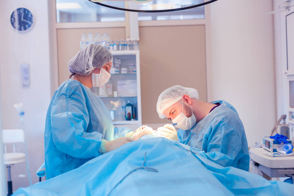 Male surgeon performs surgical procedures in the operating room, while his assistant monitors the patient condition - Photo, image
