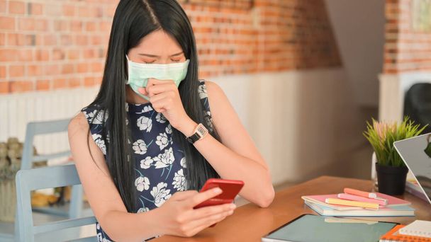 Une femme portant un masque utilise un smartphone dans un café.Elle risque d'être infectée par le virus Covid-19
. - Photo, image