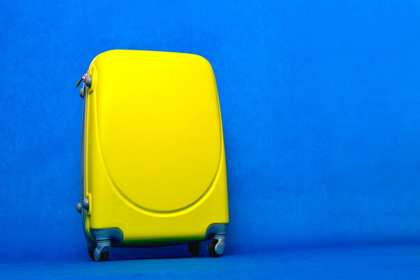 Travel bag to the wall. Yellow suitcase on a blue background. - Фото, изображение