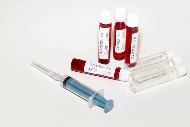 Injectiespuit met bloedmonsters en lege injectieflacons op wit tafelblad voor coronavirusonderzoek  - Foto, afbeelding