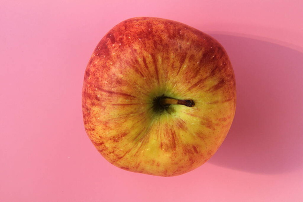 Red yellow apple on a pink background. Juicy ripe beautiful fruit - Фото, изображение