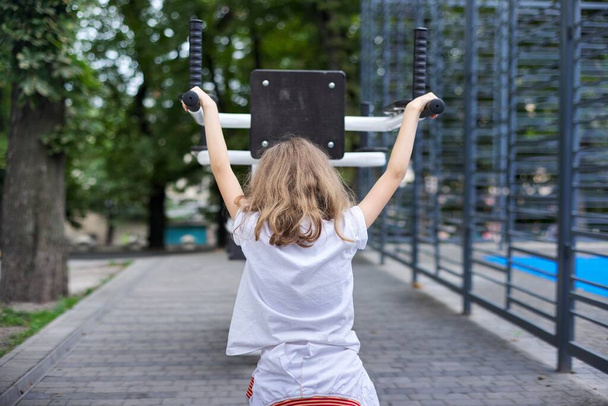 Kind meisje op sport outdoor simulator, actieve gezonde levensstijl van kinderen, stedelijke sportvelden, achteruitkijk - Foto, afbeelding