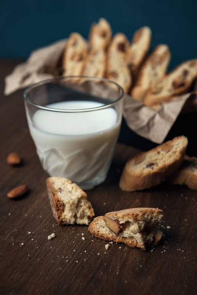 Biscotti fatti in casa italiani cantuccini con semi di mandorla in scatola di metallo su carta sgualcita marrone e bicchiere di latte
 - Foto, immagini