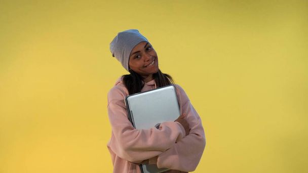 Retrato de chica africana en gorra abrazando su computadora portátil
 - Foto, Imagen