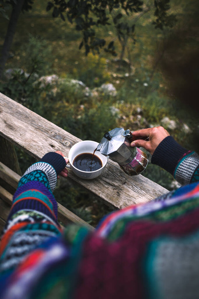 Uma mulher derrama café em uma xícara branca de uma máquina de café geyser, bebida quente da manhã na natureza, menina está fazendo café no alpendre de uma casa de madeira. - Foto, Imagem