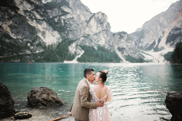 Wedding couple on the nature is hugging each other near a beautiful lake in the mountains.. Beautiful model girl in white dress. Man in suit - Photo, image
