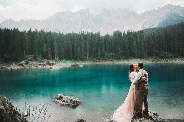 Beautiful modern couple kissing near a lake in the mountains - Фото, изображение