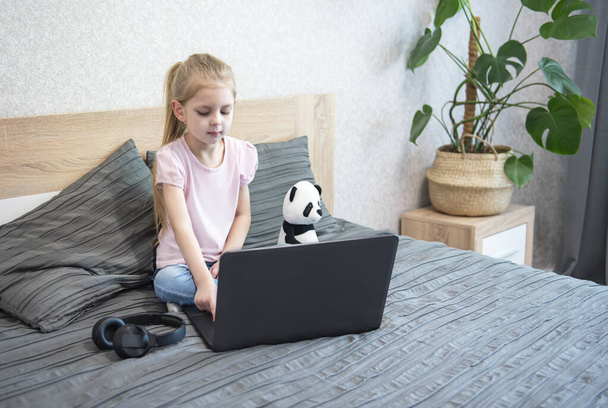 Běloška dívka dítě sedí v posteli a učí se online na notebooku. Home school, online education, home education, karanténa, coronavirus concept. - Fotografie, Obrázek