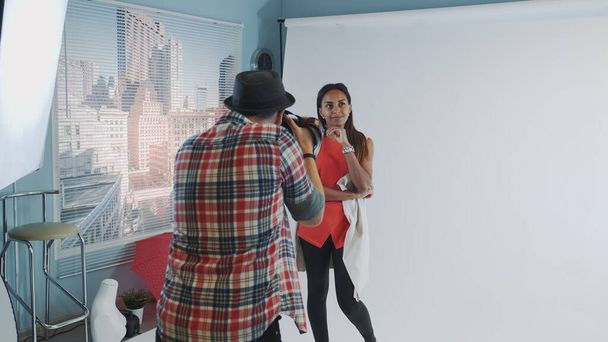 Behind the scenes on photo shoot: professional photographer working in studio by taking photos of black model - Photo, Image