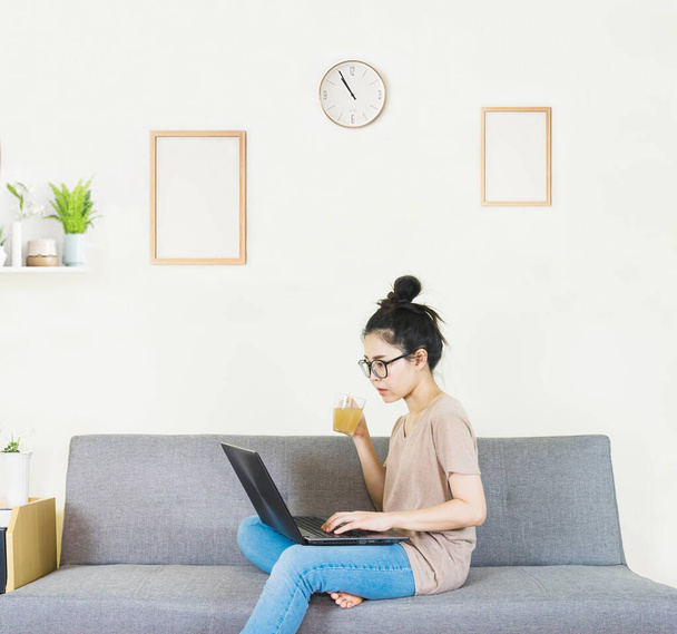 selective focus young beautiful asian woman wore glasses, brown t shirt and jean,sitting on gray sofa in living room ,work online lifestyle,relax at home with tea,home working laptop,work from home - Fotó, kép
