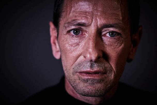 Retrato de um homem vestido de preto em um fundo escuro com um olhar sério, características duras e olhos azuis olhando em frente
 - Foto, Imagem