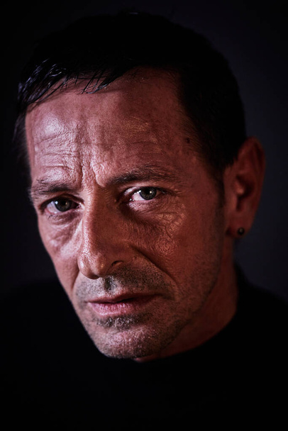 Портрет человека, одетого в черное на темном фоне с серьезным взглядом, твердыми чертами лица и голубыми глазами, смотрящими прямо вперед
 - Фото, изображение