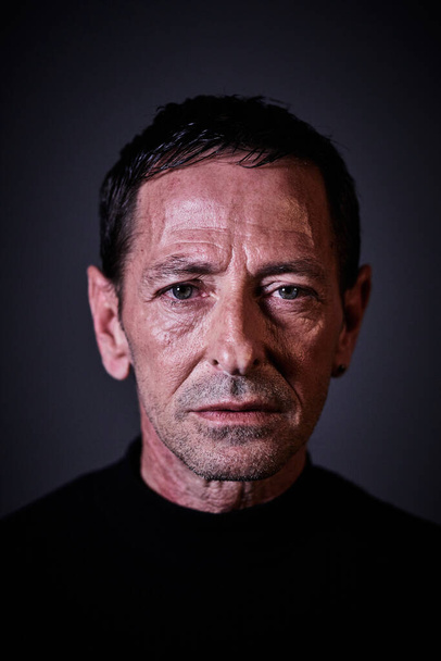 Retrato de um homem vestido de preto em um fundo escuro com um olhar sério, características duras e olhos azuis olhando em frente
 - Foto, Imagem