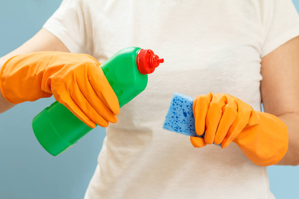 Frau im weißen T-Shirt mit einer Plastikflasche Waschmittel und einem Schwamm auf blauem Hintergrund. Wasch- und Reinigungskonzept. - Foto, Bild