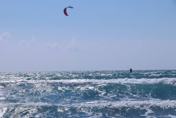 Wonderful morning day, ideal time for some activity. In the distance Kiteboarder sails on surfboard and gaining speed thanks to the parachute. Windy day with some waves in Cyprus. - Photo, Image