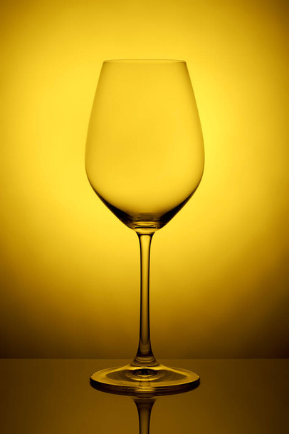 Het kristalglas staat op het spiegeloppervlak op een gele achtergrond. studiofoto. product. Prachtige schaduw van wijnglas. macro foto. - Foto, afbeelding