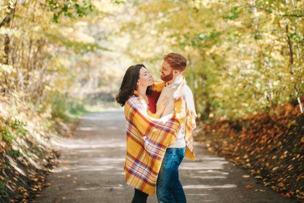 Krásná zamilovaná páreček. Usmívající se přítel a přítelkyně zabaleni ve žluté přikrývce objímající se v parku na podzim. Spolu a šťastně. Praví skuteční lidé. - Fotografie, Obrázek