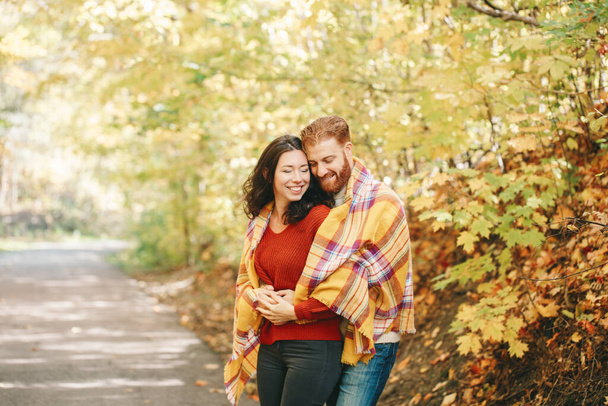 Красивая пара влюблённых мужчин. Улыбающиеся смеющиеся бойфренд и девушка, завернутые в желтое одеяло, обнимаются в парке осенним осенним днем. Сплоченность и счастье. Настоящие люди
. - Фото, изображение