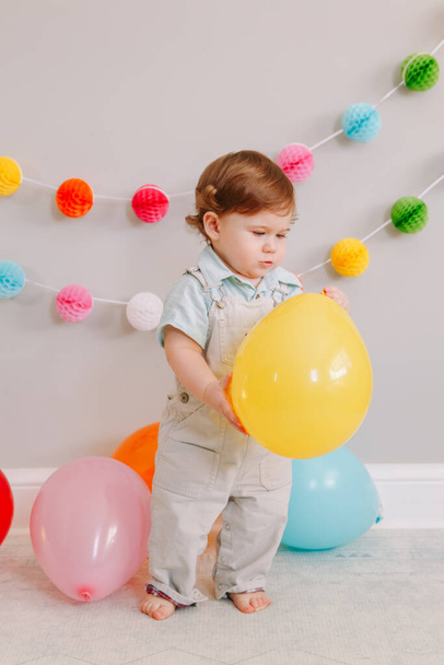 Funny Caucasian baby boy celebrating his first birthday. Excited child kid toddler playing with colorful balloons. Celebration of event or party indoors at home. Happy birthday lifestyle concept. - Foto, Imagem