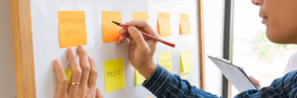 Empresários organizando notas pegajosas comentando e brainstorming sobre prioridades de trabalho colega em um espaço de co-trabalho moderno
 - Foto, Imagem