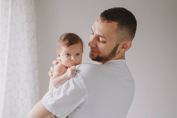 Young Caucasian bearded dad carrying newborn baby on shoulder. Male man parent  holding child daughter son in arms. Authentic family lifestyle documentary moment. Fathers Day holiday. - Photo, Image