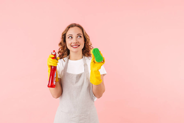 Image of cheery cute woman housewife isolated over pink wall background in gloves holding sponge an cleanser. - Valokuva, kuva
