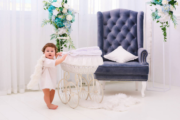 Little boy 1 year old like angel smile and stand near buggy. Toddler boy in angel wings in baroque style interior room. international children's day. - 写真・画像