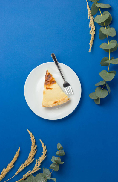 Single piece of cheesecake on a white plate on blue background. - Foto, afbeelding
