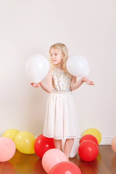 Cute adorable little girl celebrating birthday at home. Lovely girl child with colorful balloons having fun. Quarantine birthday party at home alone during COVID-19 pandemic self isolation. - 写真・画像