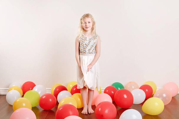 Cute adorable little girl celebrating birthday at home. Lovely girl child with colorful balloons having fun. Quarantine birthday party at home alone during COVID-19 pandemic self isolation. - 写真・画像
