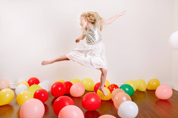 Cute adorable little girl celebrating birthday at home. Lovely girl child with colorful balloons having fun. Quarantine birthday party at home alone during COVID-19 pandemic self isolation. - Photo, Image
