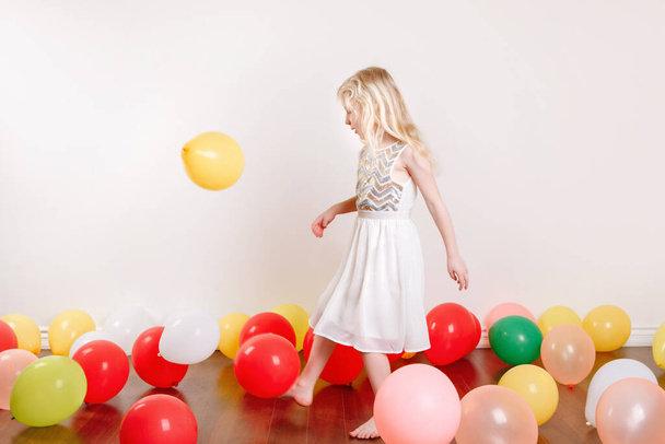 Evde doğum gününü kutlayan sevimli küçük bir kız. Renkli balonları olan güzel bir kız çocuğu eğleniyor. COVID-19 salgını sırasında evde tek başına karantina doğum günü partisi. - Fotoğraf, Görsel
