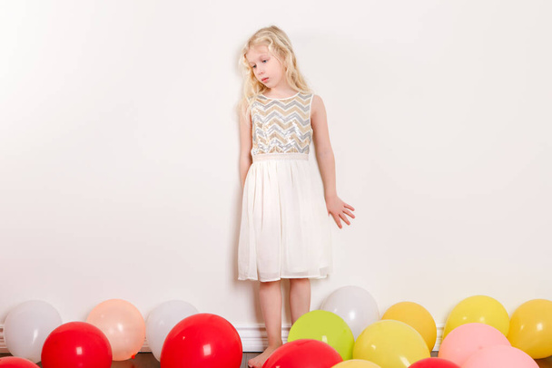 Λυπημένο αναστατωμένο κοριτσάκι γιορτάζει τα γενέθλιά του στο σπίτι. Υπέροχο μοναχικό δυστυχισμένο κορίτσι με πολύχρωμα μπαλόνια. Πάρτι γενεθλίων καραντίνας στο σπίτι μόνο κατά τη διάρκεια της πανδημίας αυτοαπομόνωσης COVID-19. - Φωτογραφία, εικόνα