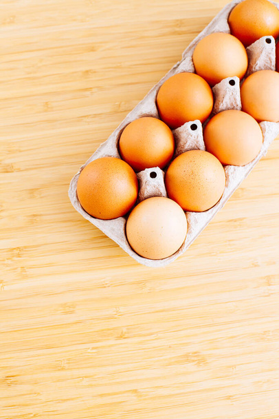 Overhead view of fresh brown chicken eggs in open egg carton box on wooden table background. Top view with copy space. Natural healthy food and organic farming concept. - Φωτογραφία, εικόνα