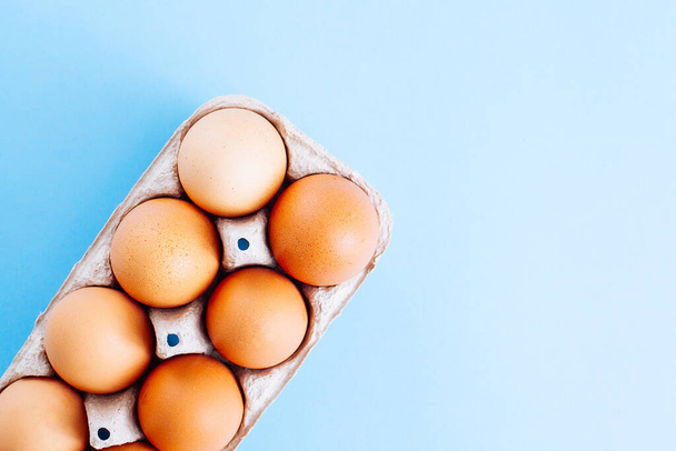 Overhead view of fresh brown chicken eggs in open egg carton box on blue background. Top view with copy space. Natural healthy food and organic farming concept. - Fotografie, Obrázek