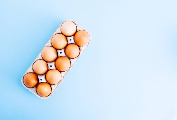 Overhead view of fresh brown chicken eggs in open egg carton box on blue background. Top view with copy space. Natural healthy food and organic farming concept. - Φωτογραφία, εικόνα
