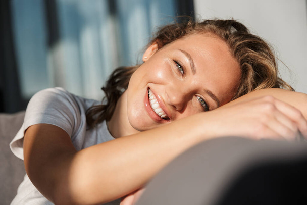 Smiling pretty blonde young woman wearing casual clothes relaxing on a couch at home - Zdjęcie, obraz